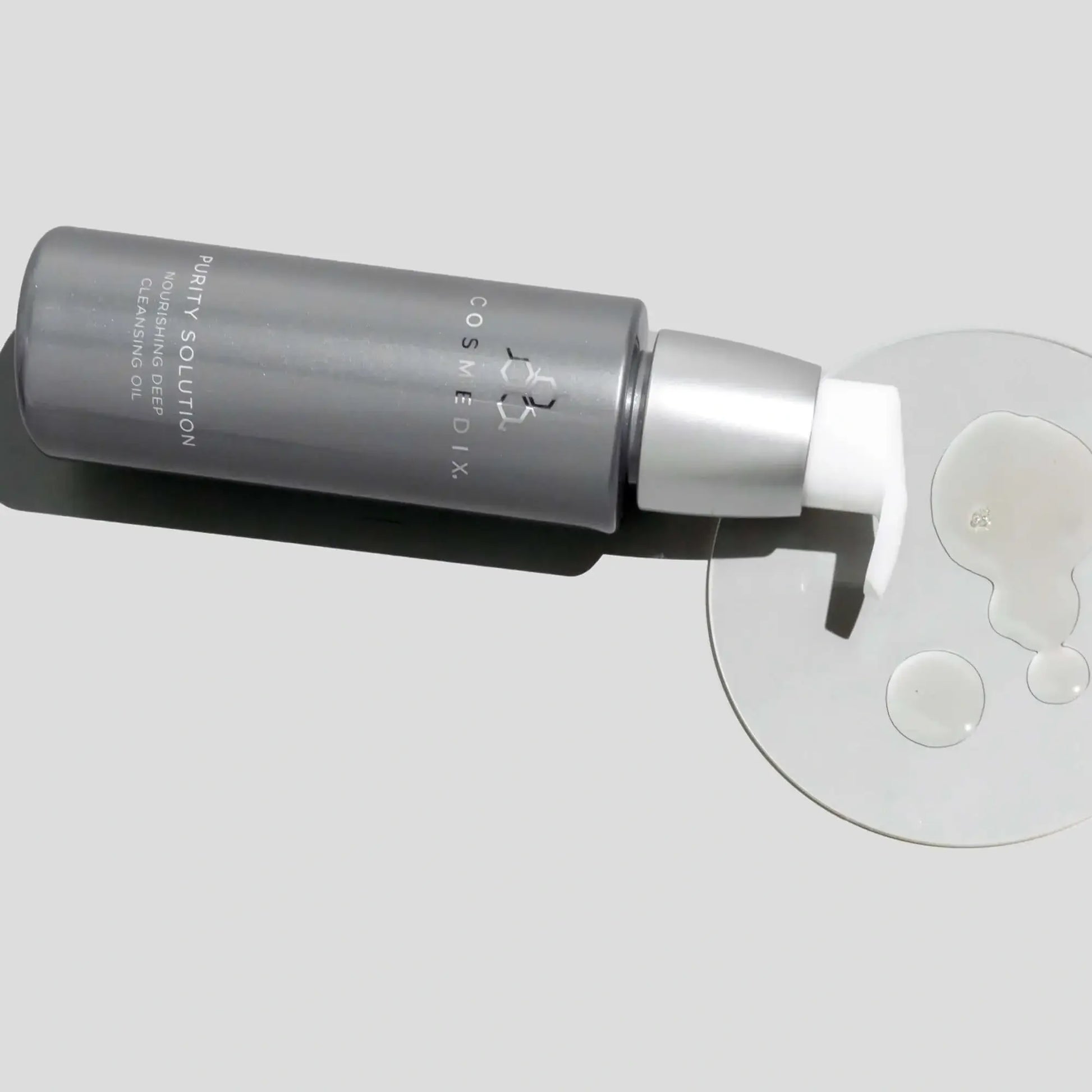 Cosmedix Purity Solution Nourishing Cleansing Oil 100ml op een lichte ondergrond met een druppel olie ernaast.